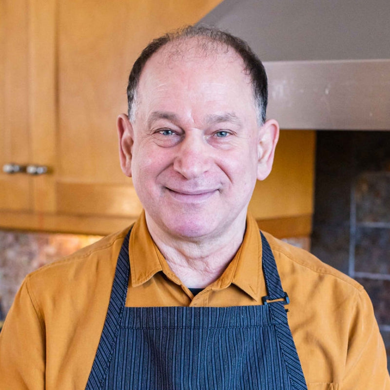 Man wearing a mustard shirt and blue apron in a kitchen setting