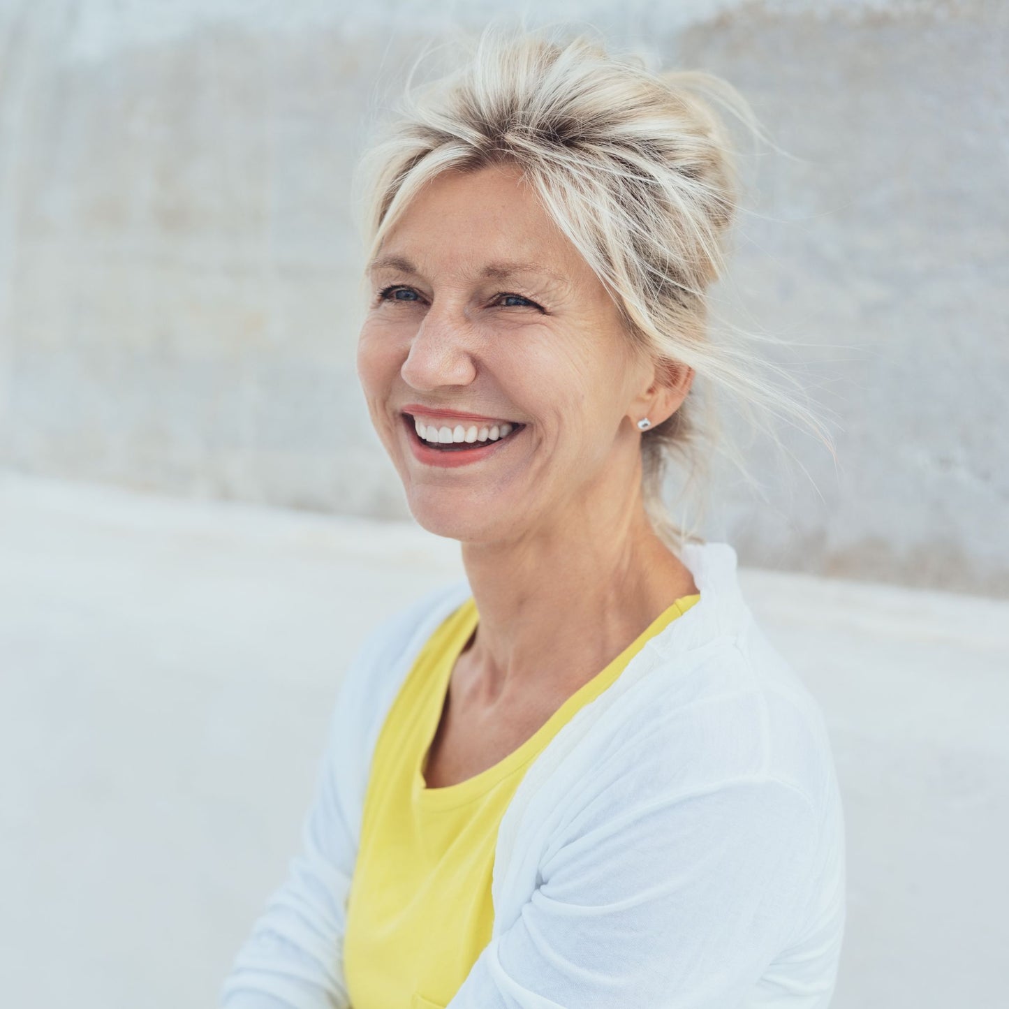 Woman with blonde hair wearing a yellow top and white cardigan against a light background