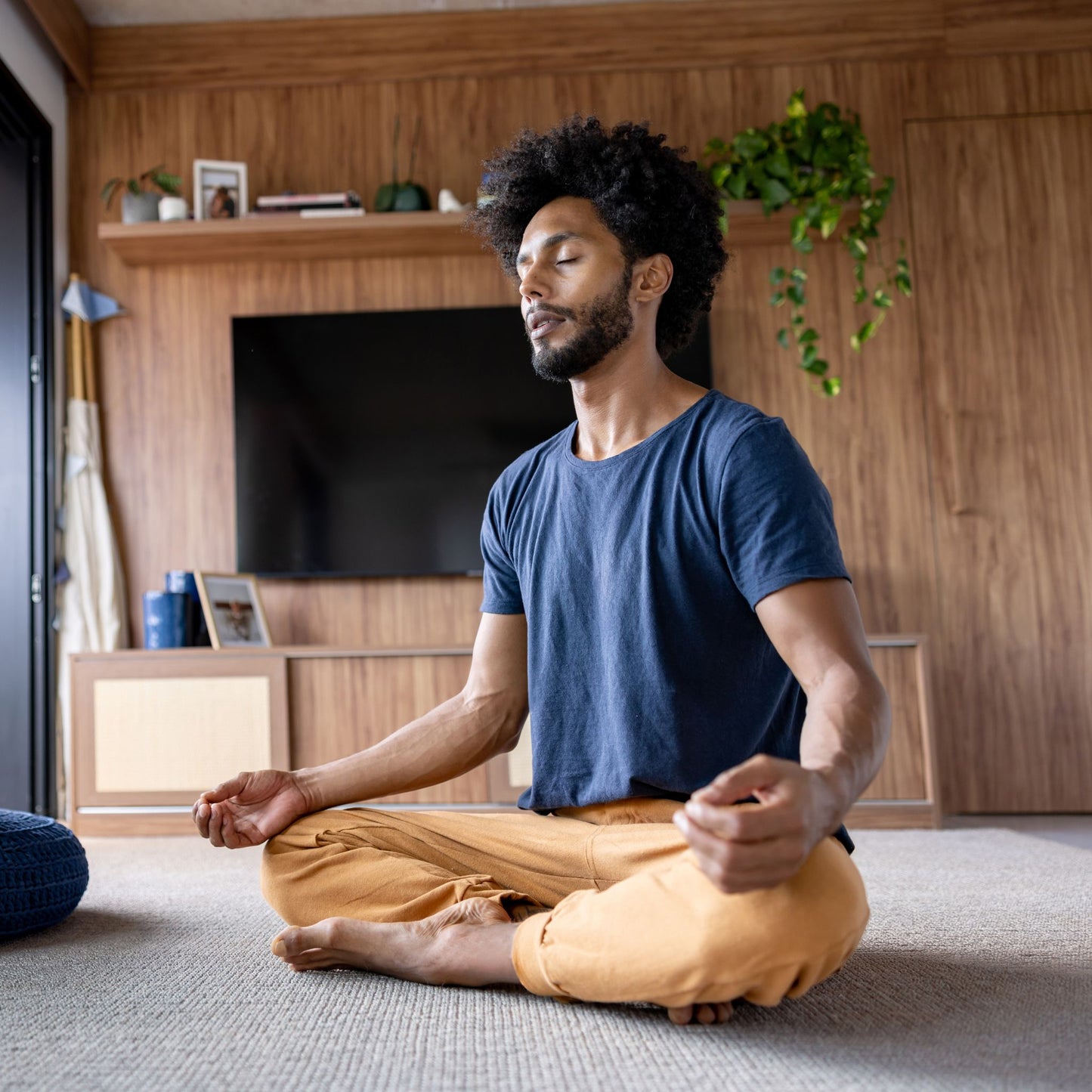 Man meditating in a living room with wooden walls and a TV.