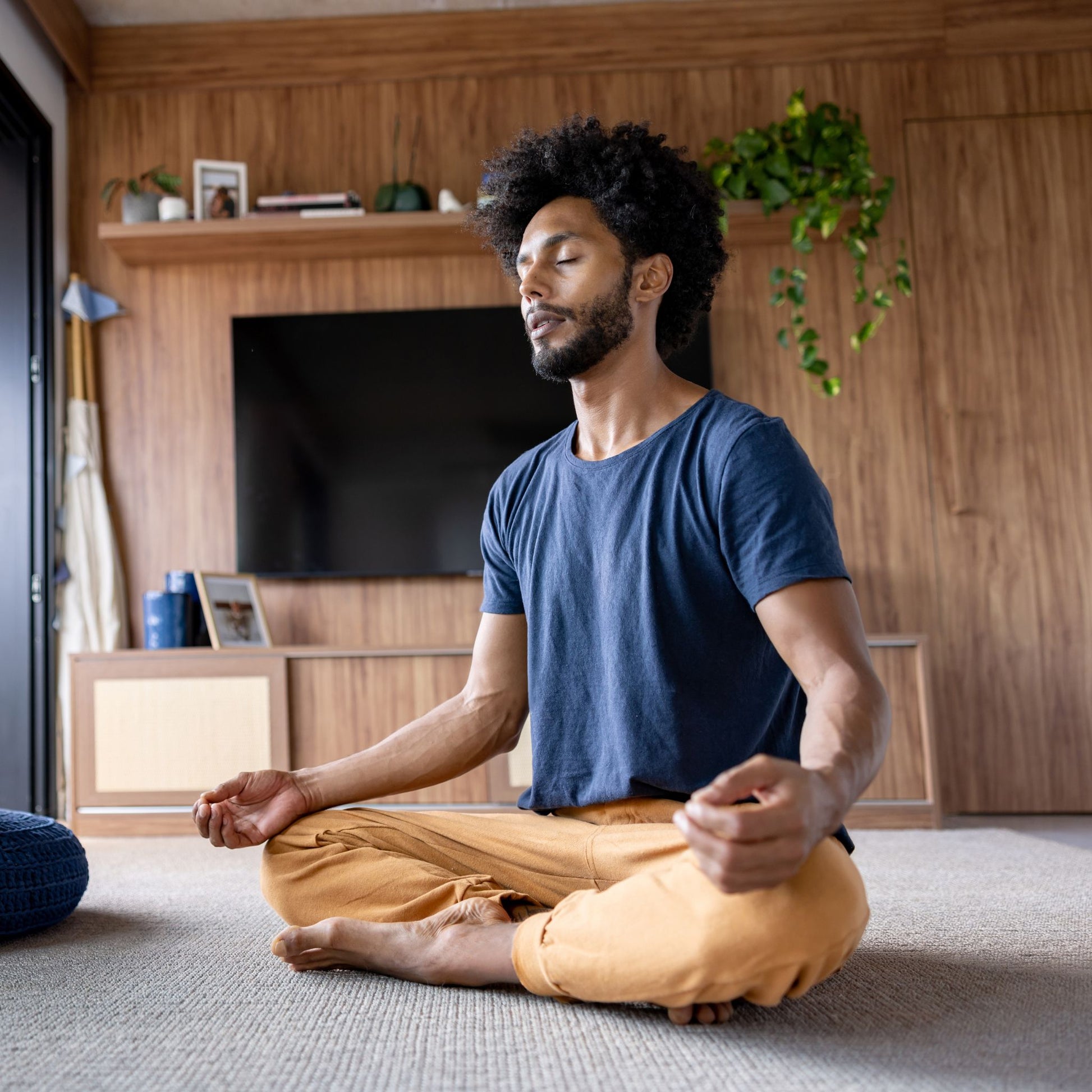 Man meditating in a living room with wooden walls and a TV.