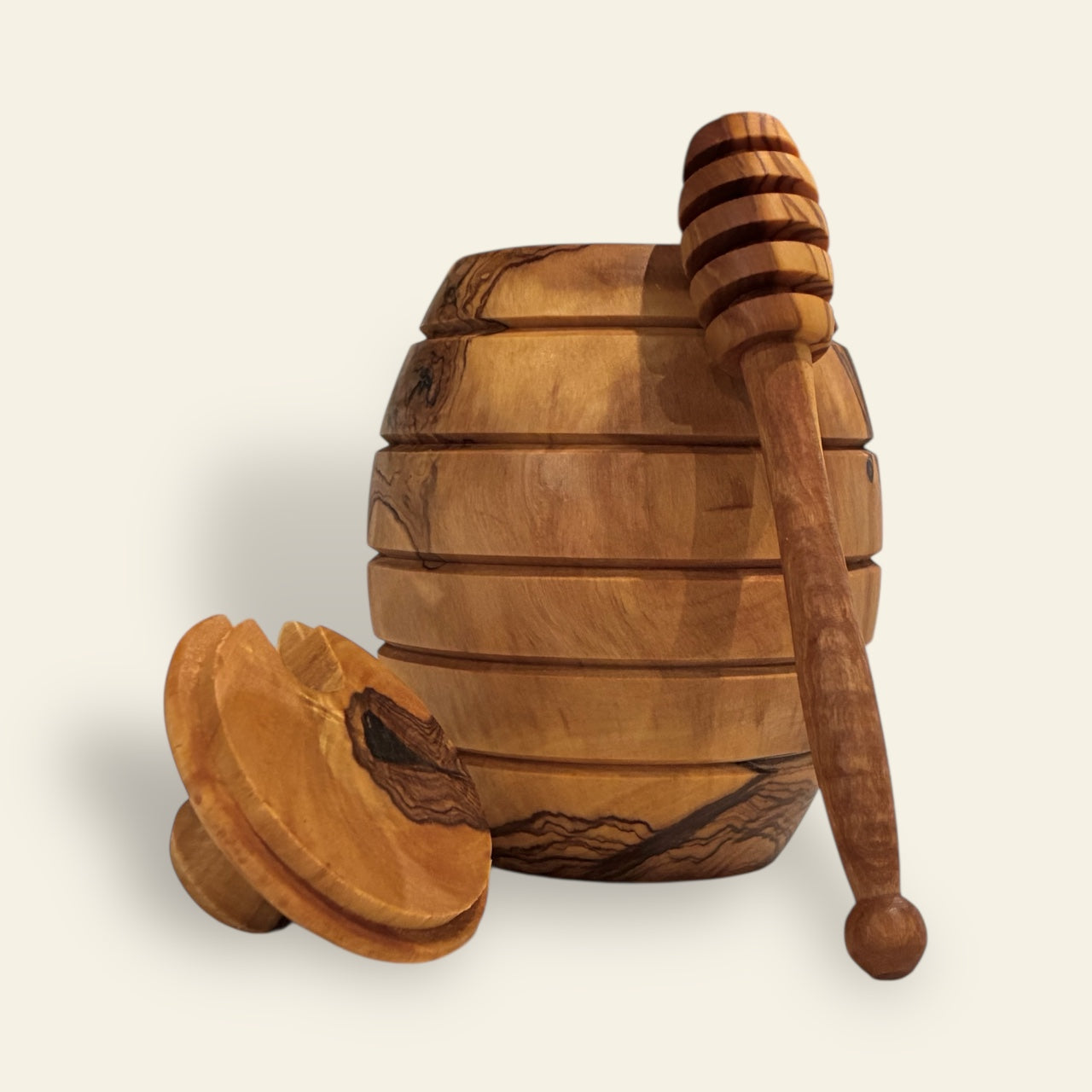 All's Well Teas and Elixirs - Honey dipper leaning against a light brown olive wood honey pot on a beige background.