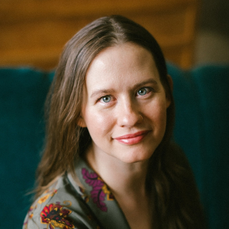 Woman with long brown hair wearing a patterned top sitting on a teal couch